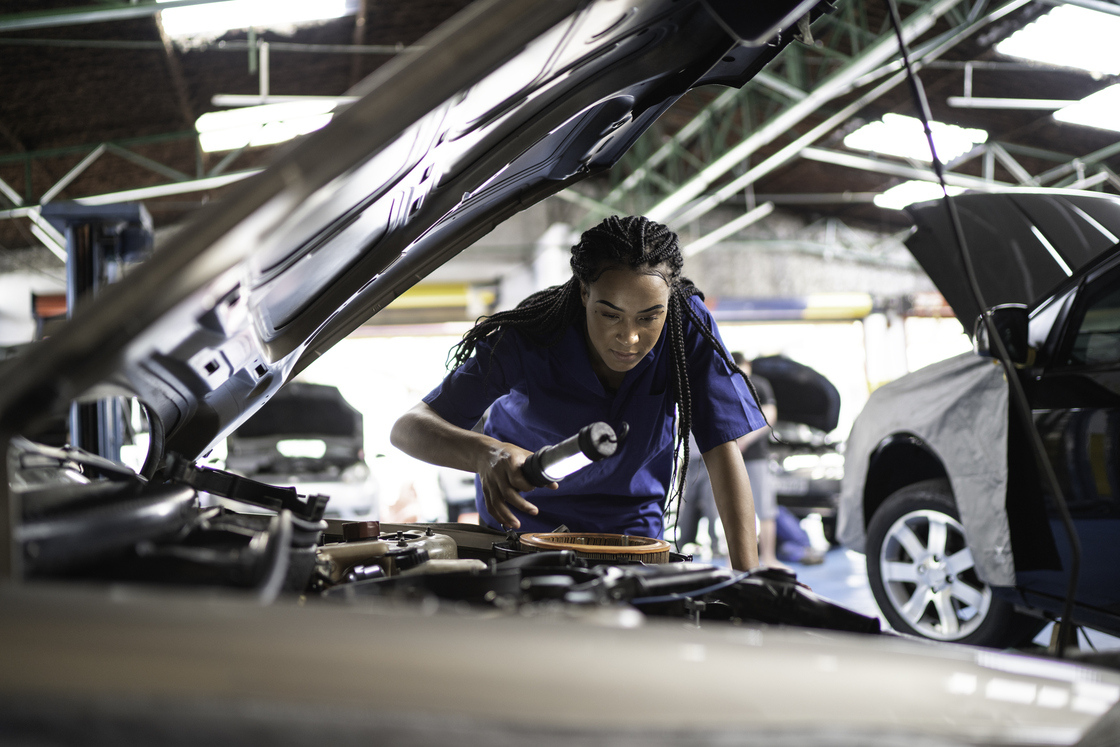 Mulher mecânica trabalhando em um carro, verificando o motor com ferramentas em uma oficina, foco em manutenção automotiva eficiente.