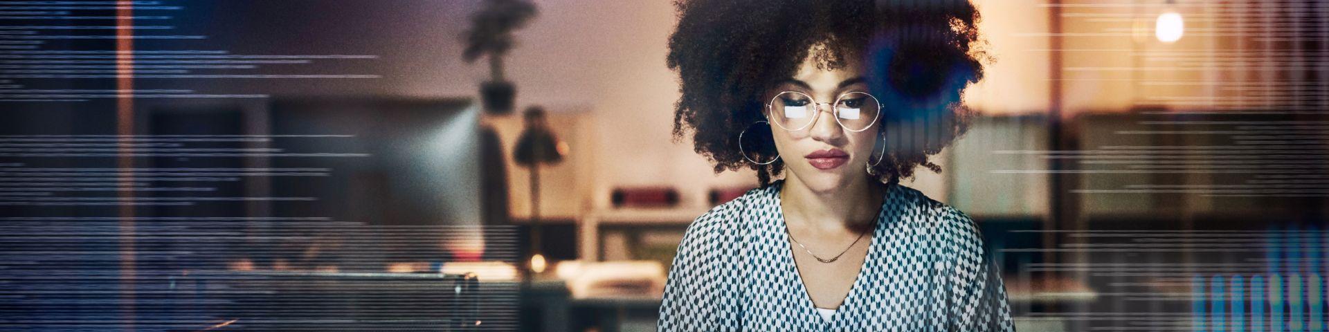 Jovem profissional de óculos com cabelo afro em um ambiente de escritório, usando blusa de poá, simbolizando tecnologia, inovação e trabalho remoto.