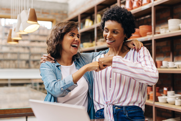 Duas mulheres sorrindo e se abraçando em um ambiente acolhedor, representando amizade e felicidade em um momento descontraído.