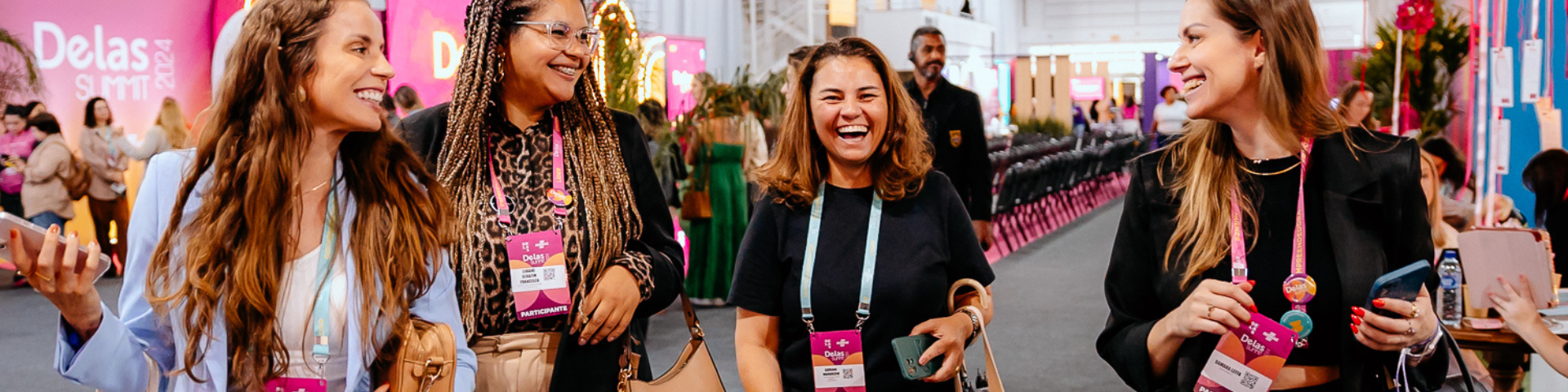 Mulheres sorridentes no Delas Summit 2024, conversando e trocando ideias em um ambiente moderno e bem decorado.