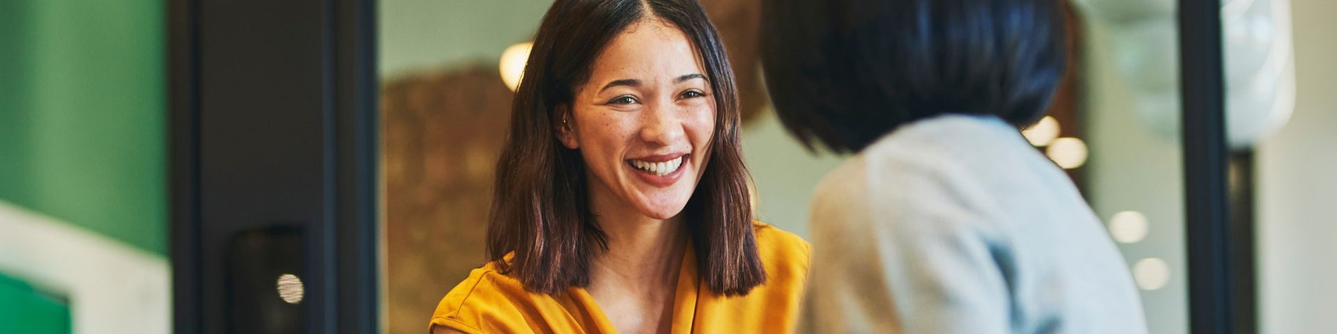 Duas mulheres trocam experiências em um ambiente corporativo. Uma delas sorri com entusiasmo, representando o poder da troca de ideias e do networking para fortalecer a jornada empreendedora.