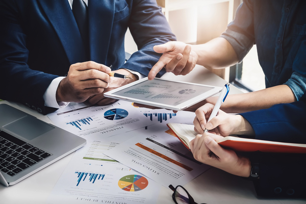 Reunião de negócios com pessoas discutindo gráficos e estratégias em uma mesa. A imagem representa trabalho colaborativo e análise de dados.