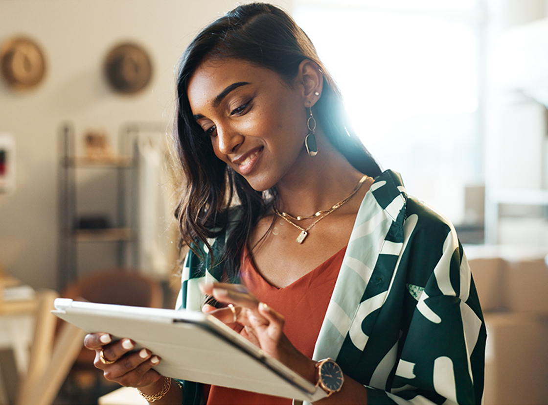 Mulher jovem sorrindo enquanto utiliza um tablet em um ambiente moderno, demonstrando interesse e tecnologia no dia a dia.
