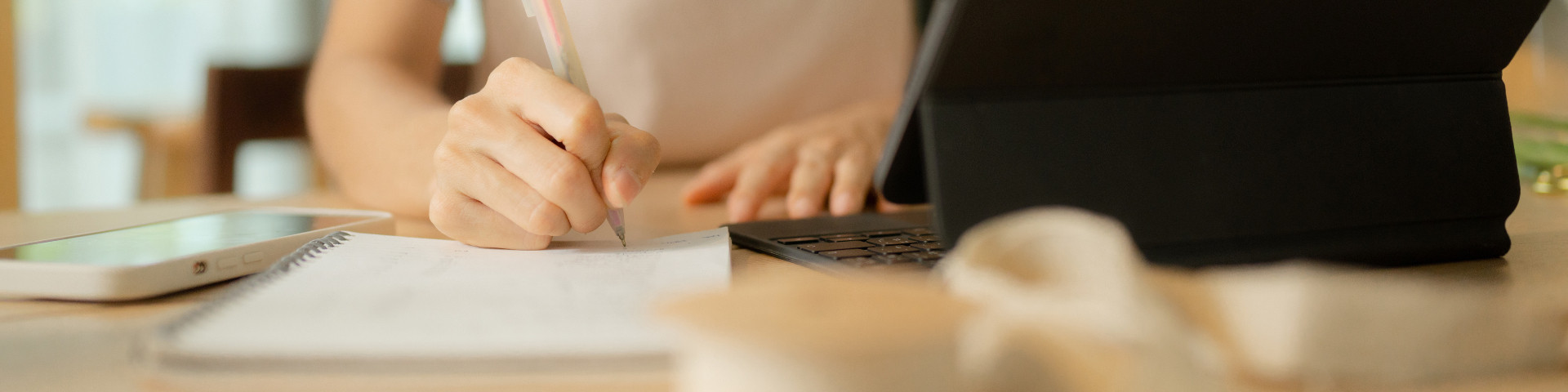 Pessoa trabalhando em uma mesa com laptop, anotações e celular, focada em tarefas de escritório ou trabalho remoto.