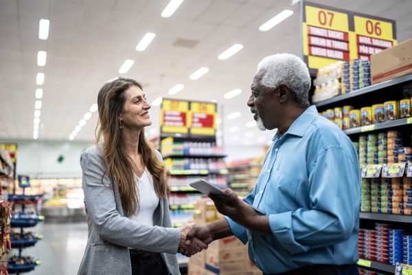 Uma mulher e um homem conversam e se cumprimentam em um supermercado, demonstrando um momento de cordialidade e interação social.