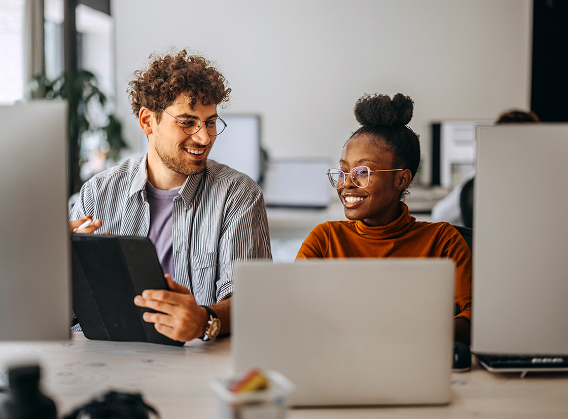 Dois profissionais conversando e sorrindo em um ambiente de escritório moderno, destacando a colaboração e a interação no trabalho.