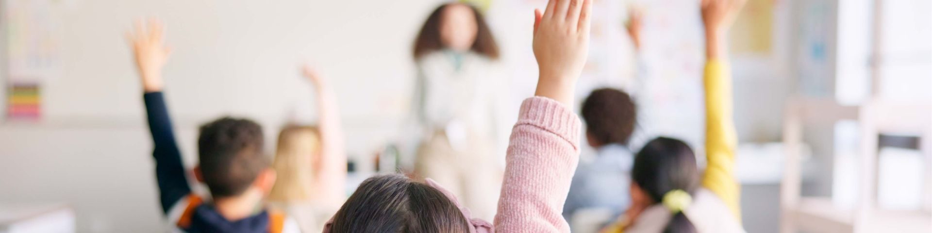 Crianças em sala de aula participando de aula interativa, com destaque para uma criança levantando a mão, promovendo aprendizado e engajamento escolar.