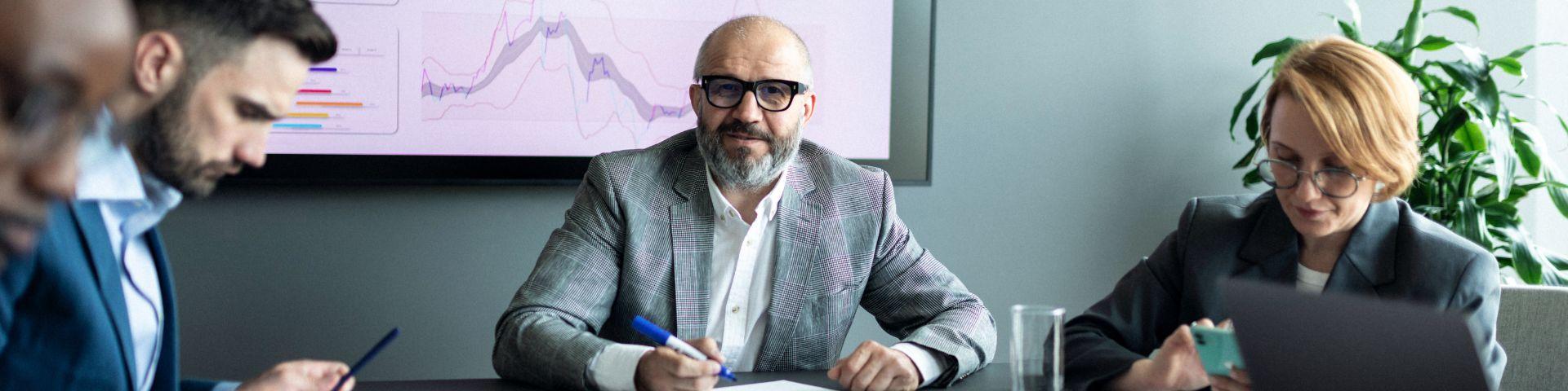Reunião de negócios com executivos analisando gráficos em tela, representando a avaliação de métricas e indicadores como o ROI para decisões estratégicas.