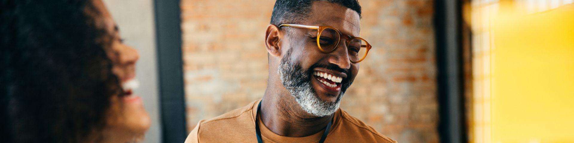 Homem sorridente, em conversa descontraída com colegas em um ambiente de trabalho.