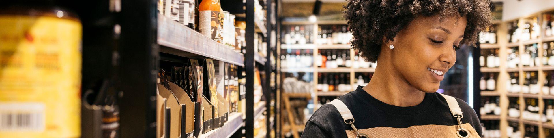 Empreendedora em mercado local analisando produtos na prateleira, representando inovação social e valorização de pequenos negócios.