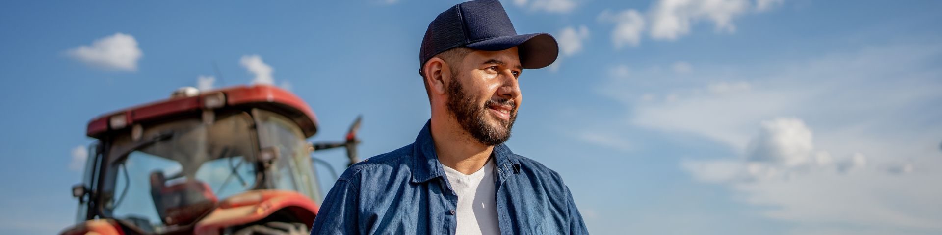 Agricultor observa a lavoura ao lado de trator moderno, simbolizando o uso de máquinas e tecnologias que impulsionam a produtividade no agronegócio.