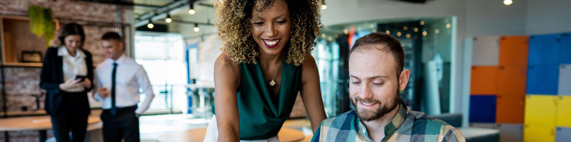 Mulher sorridente com cabelo cacheado e homem com barba sorrindo enquanto trabalham juntos em uma ambiente de escritório moderno