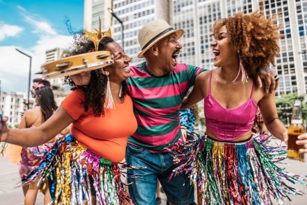 Três pessoas se divertindo em uma festa de carnaval, com roupas coloridas e alegres. Elas estão dançando e sorrindo, celebrando a cultura brasileira.